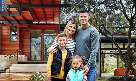 Fort Worth family of four smiling in front of home with custom iron doors and windows